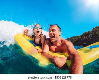 Father and daughter having fun in the sea and getting splashed by the big waves while floating on the inflatable yellow airbed - Powered by Shutterstock