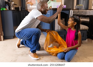 Father and daughter high-fiving while collecting trash in kitchen together. Family, teamwork, environment, cleaning, bonding, recycling - Powered by Shutterstock