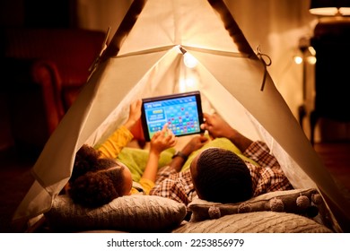 Father And Daughter At Home Lying In Indoor Tent Or Camp Gaming On Digital Tablet - Powered by Shutterstock