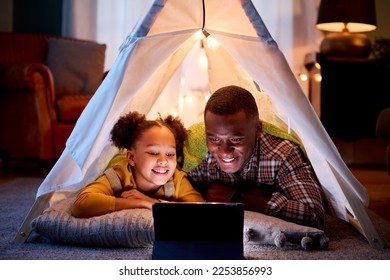 Father And Daughter At Home Lying In Indoor Tent Or Camp Watching Or Streaming To Digital Tablet - Powered by Shutterstock