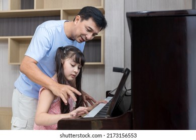 Father and daughter at home playing music on a piano. Dad and daughter are playing the piano. Pianist teacher teaching girl kid student to play piano, music education concept. - Powered by Shutterstock