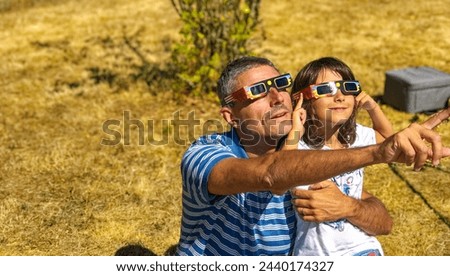 Father and daughter looking at the sun during a solar eclipse on a country park, family outdoor activity.