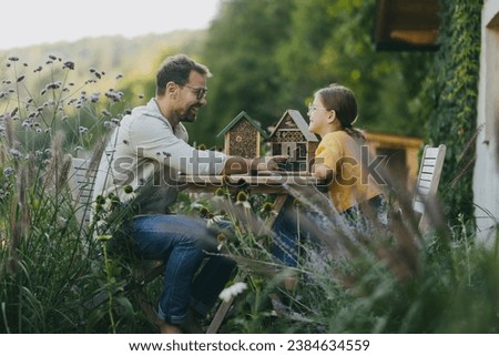 Father with daughter making bug hotel, or insect house outdoors in the garden. Girl learning about insects, garden ecosystem and biodiversity.