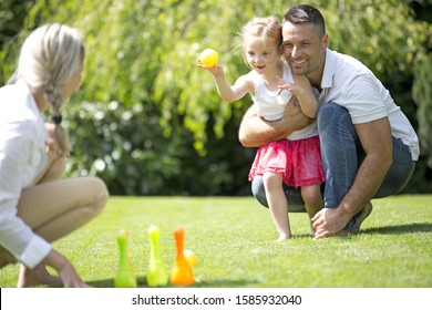 Father and daughter playing on lawn with skittles and ball