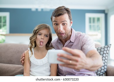 Father And Daughter Pulling Funny Faces While Taking Selfie In Living Room At Office