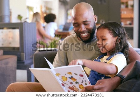 Father And Daughter Reading Book At Home Together With Multi-Generation Family In Background