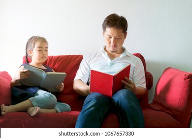 Father And Daughter Are Reading Books.Sitting On A Red Sofa.It Is A Good Learning Practice And A Good Family Relationship.Golden Light Shining.Like New Things Good Things Are Coming.