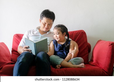 Father And Daughter Are Reading Books.Sitting On A Red Sofa.It Is A Good Learning Practice And A Good Family Relationship.light Shining.Like New Things Good Things Are Coming.