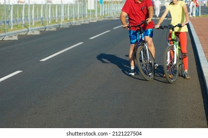 Father And Daughter Riding Bicycles On The Street. A Father And Daughter Ride  Bikes On A City Road In A Stadium. No Faces. 