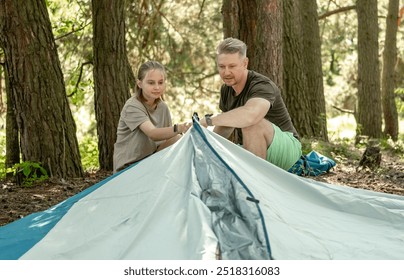 Father And Daughter Setting Up A Tent While Camping In The Forest - Powered by Shutterstock