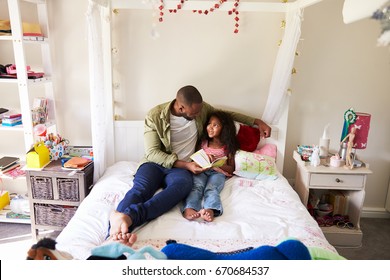 Father And Daughter Siting On Bed Reading Book Together