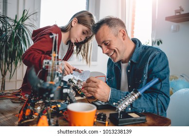 Father and daughter sitting by the wooden table at workshop building robot as a school science project and having fun