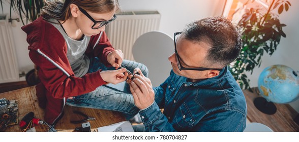 Father And Daughter Sitting By The Wooden Table And Building Robot At Home As A School Science Project