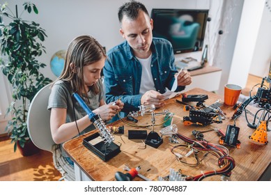 Father And Daughter Sitting By The Wooden Table And Building Robot At Home As A School Science Project