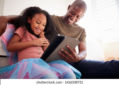 Father With Daughter Sitting On Bed In Childs Bedroom Using Digital Tablet Together
