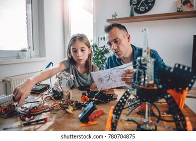 Father and daughter sitting at wooden table and together looking at electronic schematics at home workshop as a school science project - Powered by Shutterstock