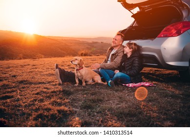 Father and daughter with small yellow dog camping on a hill while sitting on the ground by the car and having relaxing conversation