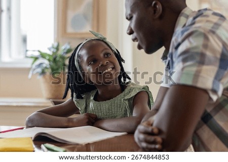 Father and daughter smiling while doing homework together at home. Family, bonding, learning, education, parenting, studying