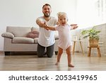 Father and daughter spending quality time together.A child learning to walk. Bearded man with his adorable blonde toddler. Close up, copy space for text, background.