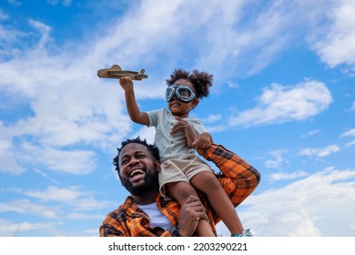 A Father And Daughter Spending Time Together. His Daughter Is Sitting On His Shoulder While Holding A Paper Aeroplane.