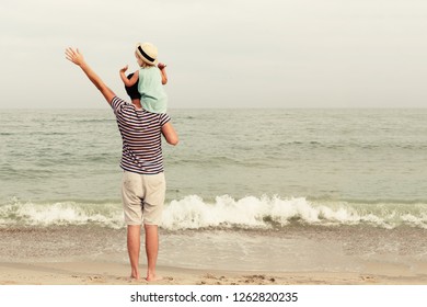 Father and daughter stand on the beach and look at the sea. Back view, copy space. - Shutterstock ID 1262820235