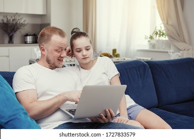 Father and daughter teenager in white t-shirts are sitting on the sofa with a laptop. Joint homework classes. Home idyll. Selective focus. Blur background. - Shutterstock ID 1727833579