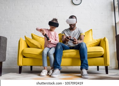 father and daughter in vr headsets playing video games on couch at home - Powered by Shutterstock