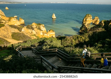 A father and daughter walk along the boardwalk on Costa Vicentina, with dramatic rock formations rising from the ocean on a sunny Algarve day. - Powered by Shutterstock