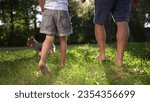 father and daughter walking in the park. happy family childhood dream concept. dad and daughter holding hands and walk barefoot on the grass. lifestyle dog running around. bare feet close up