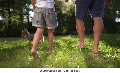 father and daughter walking in the park. happy family childhood dream concept. dad and daughter holding hands and walk barefoot on the grass. lifestyle dog running around. bare feet close up