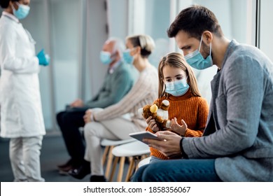 Father and daughter wearing protective face masks while surfing the net on digital tablet in a hallway at the hospital. 