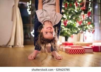 Father with daugter at Christmas tree holding her upside down.