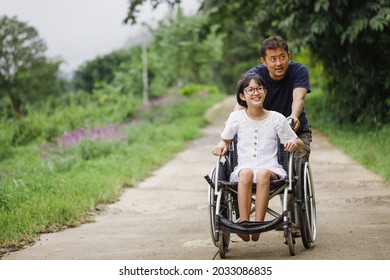 Father And Disabled Child On Wheelchair Walking On Trail Park In Sunny Day. Happy Disability Kid Travel In Family Holiday Concept.