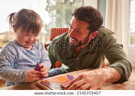 Father With Down Syndrome Daughter Playing Game With Wooden Shapes At Home Together