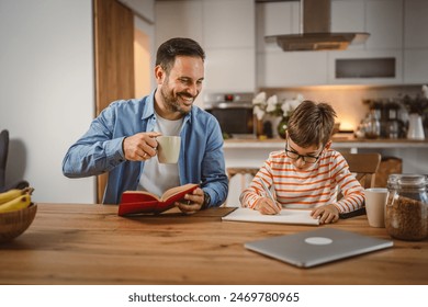 Father drink coffee and hold book while son do homework at home - Powered by Shutterstock