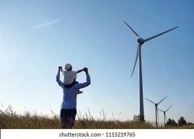 A father engineer, holds his daughter in his arms and runs between the wind turbines with great freedom. Concept of: environmental engineering, renewable energy and love for nature and for the family