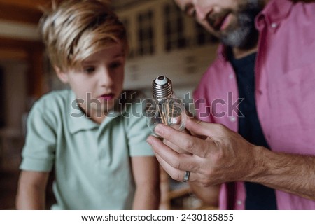 Father explaining led bubls to son, teaching him about energy efficiency, longevitiy and environmental impact. Changing bulbs at home.