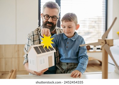 Father explaining renewable energy, teaching about sustainable lifestyle his young son. Playing with house with solar panels, wind turibine at home. - Powered by Shutterstock