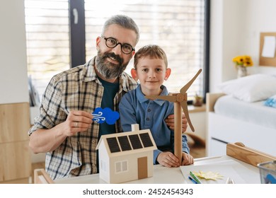 Father explaining renewable energy, teaching about sustainable lifestyle his young son. Playing with house with solar panels, wind turibine at home. - Powered by Shutterstock