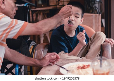 Father Feeding Food To Disabled Child On The Wheelchair In Home Or Restaurant,He Practiced Eating Food,Special Children's Lifestyle,Lifestyle In The Education Age Of Kids,Happy Disability Kid Concept.