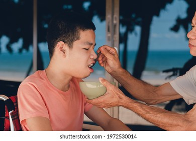 Father Feeding Food To Disabled Child On The Wheelchair In Home Or Restaurant,He Practiced Eating Food,Special Children's Lifestyle,Lifestyle In The Education Age Of Kids,Happy Disability Kid Concept.