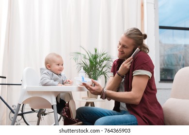 father feeding his little son with baby food while talking on smartphone - Powered by Shutterstock