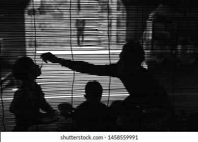 Father Feeding His Young Son With A Spoon. Sillouette Of A Asian Family In Backlight Behind A Curtain. 