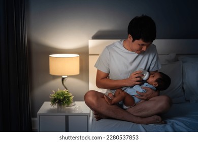 father feeding milk bottle to her newborn baby on a bed at night - Powered by Shutterstock