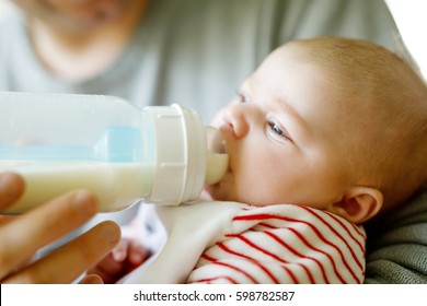 Father Feeding Newborn Baby Daughter With Milk In Nursing Bottle. Formula Drink For Babies. New Born Child, Little Girl Laying In Bed. Family, New Life, Childhood, Beginning, Bottle-feeding Concept.