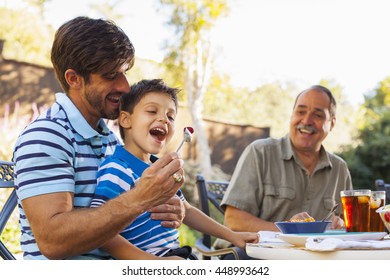 Father feeding son on lap, grandfather in background