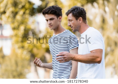 father gesturing and talking with teenager son in park