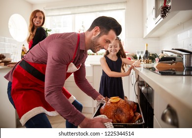 Father Getting Turkey Out Of Oven As Family Celebrate Christmas At Home Together