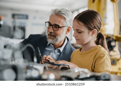 Father and girl during kid at work day, encouraging girl in career in robotics. Teacher showing young schoolgirl how to assemble small robot. - Powered by Shutterstock