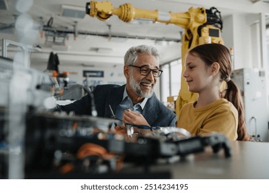 Father and girl during kid at work day, encouraging girl in career in robotics. Teacher showing young schoolgirl how to assemble small robot. - Powered by Shutterstock